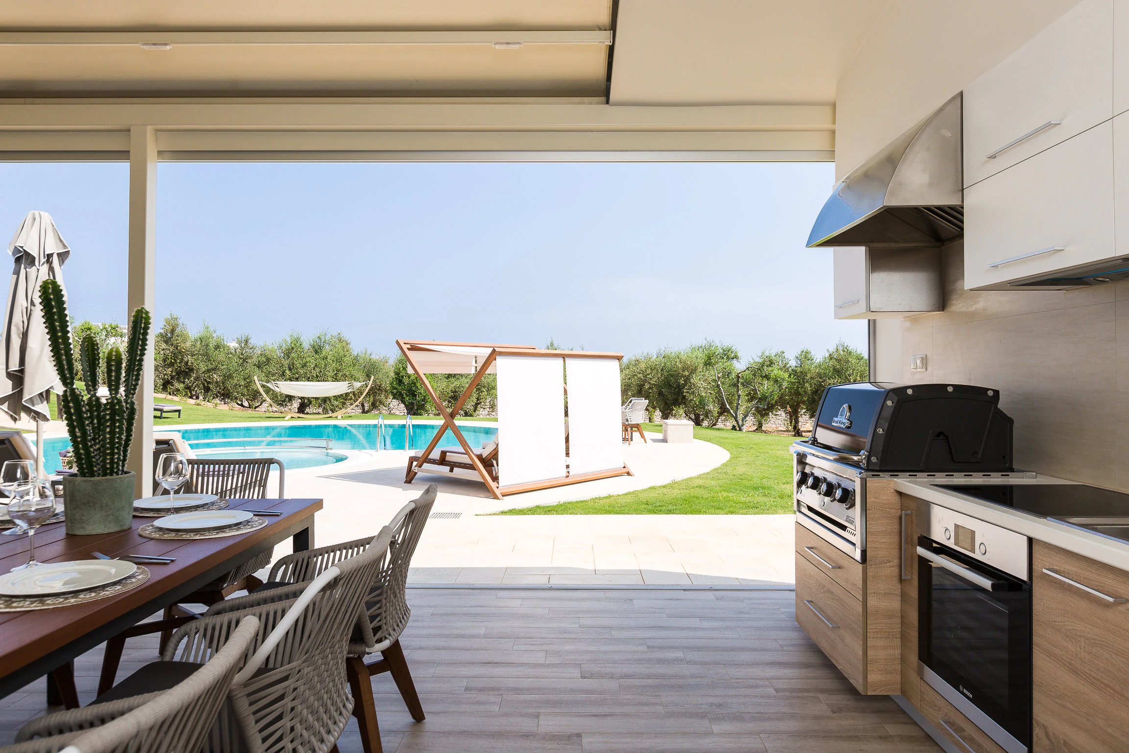 Outdoor kitchen opening toward the pool and garden