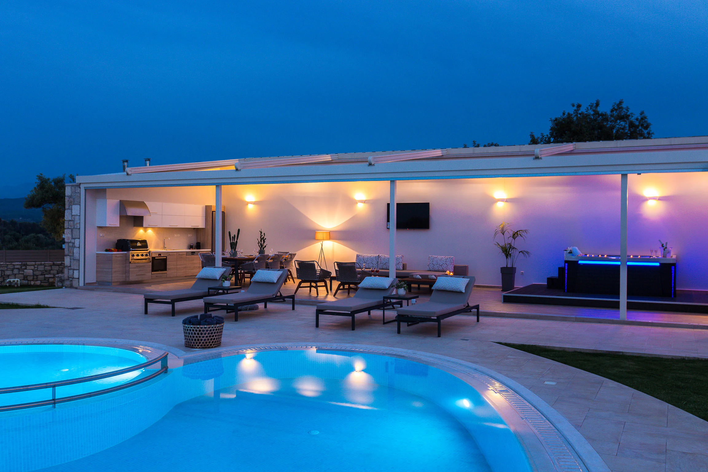 The poolside pavilion and heated spa lit at night beside the illuminated pool