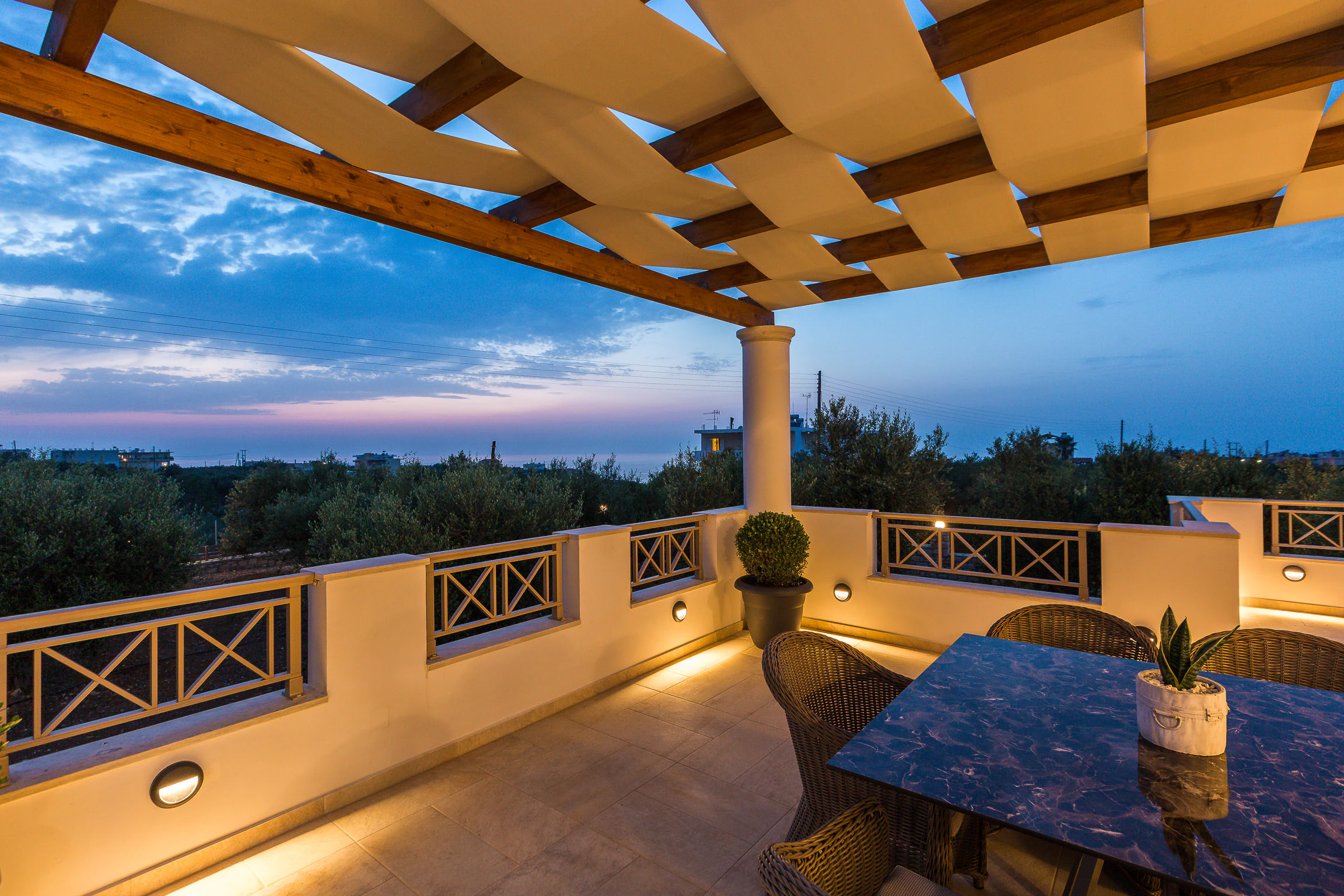 The upper terrace under its timber pergola at dusk, with floor lighting and a deep blue sky
