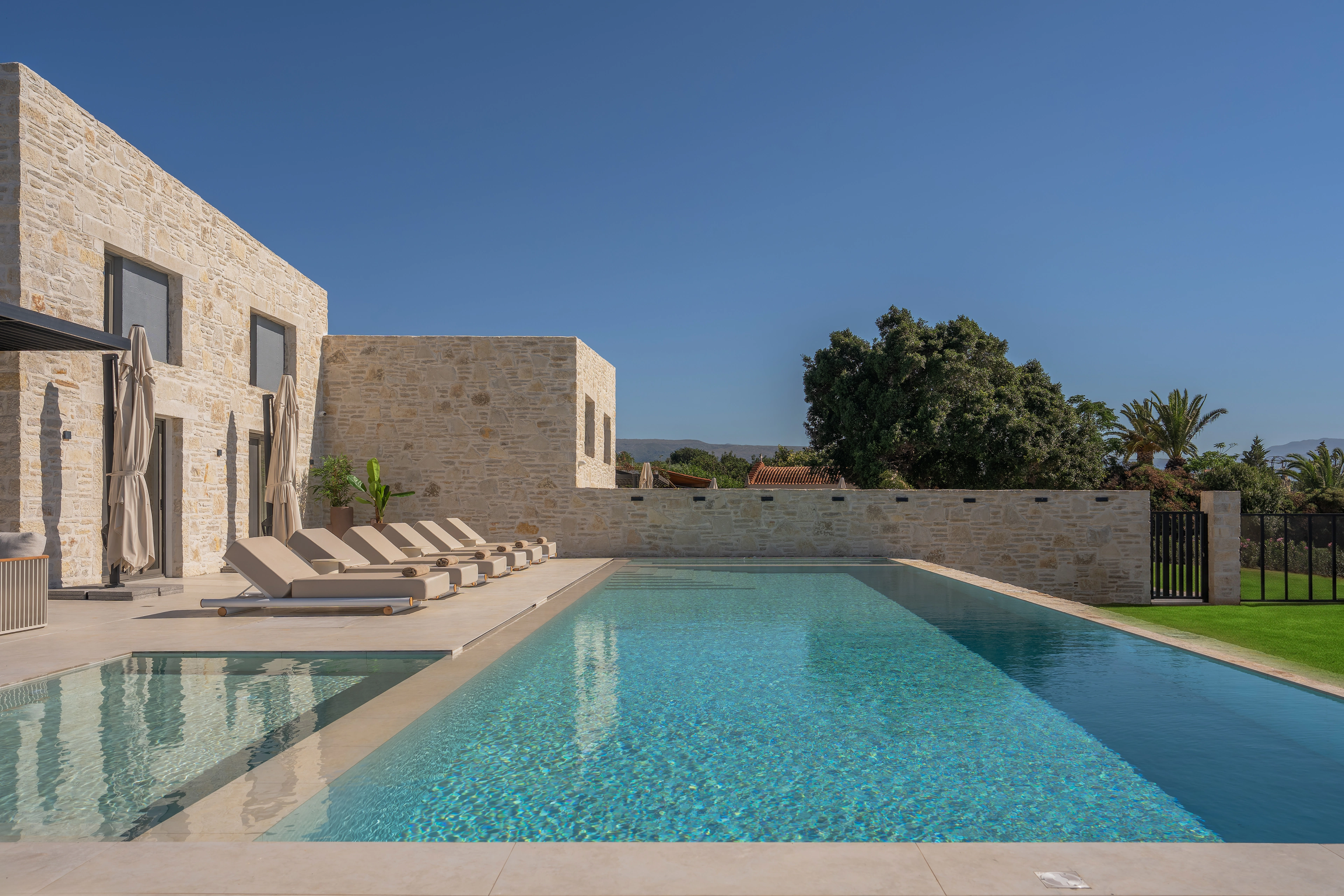 Right Crete's private pool, stone facade and row of loungers in daylight
