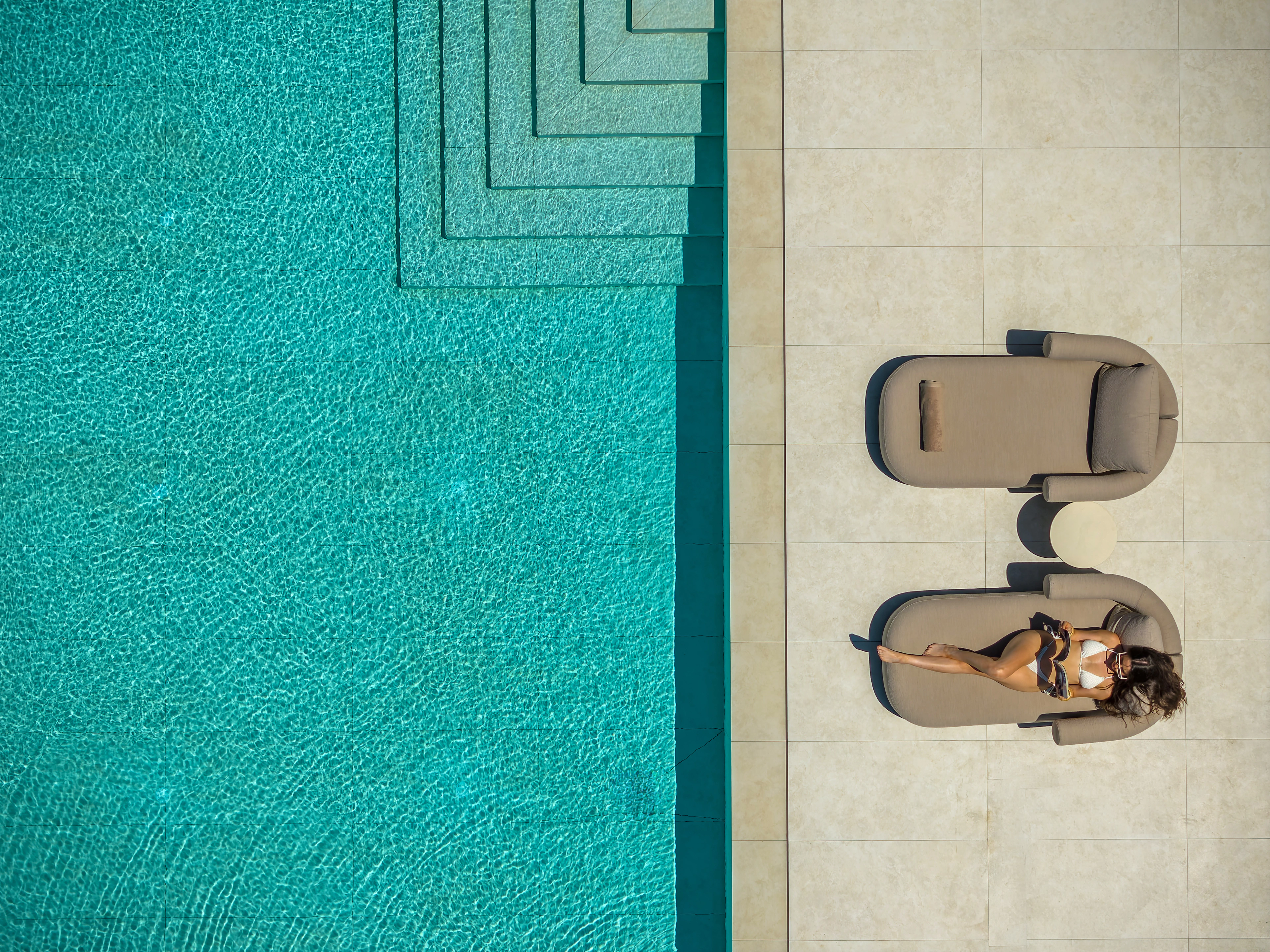A guest relaxing beside Left Crete's turquoise pool from above