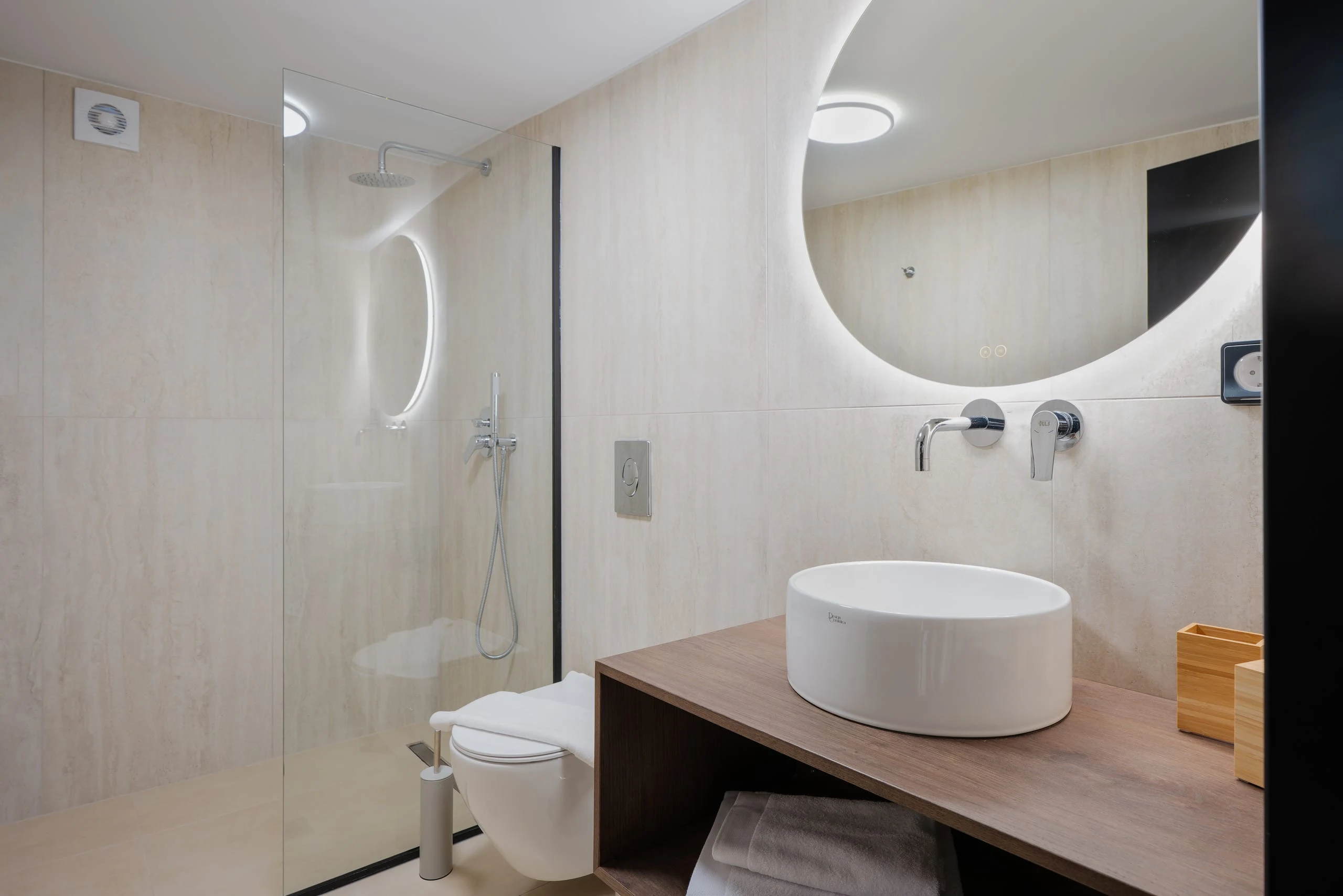 Private en-suite bathroom for Left Crete bedroom 04 with a round mirror, stone vanity and walk-in shower